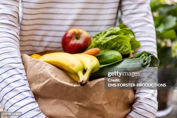 young teenager is carrying one paper bag of vegetables  at home - teenager boy shopping stock pictures, royalty-free photos & images