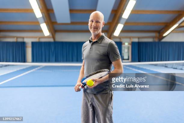portrait of a happy mid-adult man playing tennis on indoor court - ポロシャツ ストックフォトと画像
