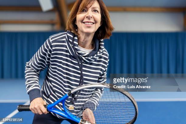happy senior woman playing tennis on indoor court - tennis racket stock-fotos und bilder