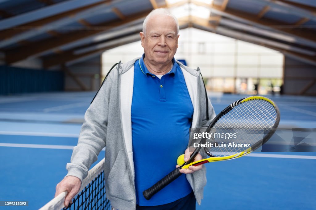 Portrait of a happy senior man playing tennis on indoor court
