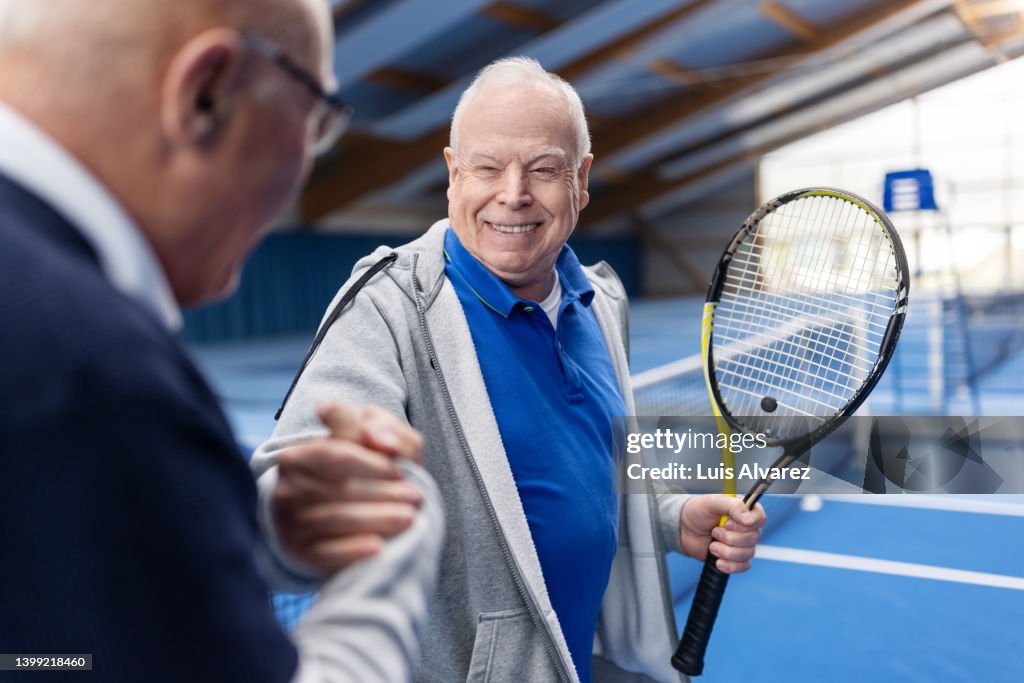 Two senior tennis players shaking hands on tennis court