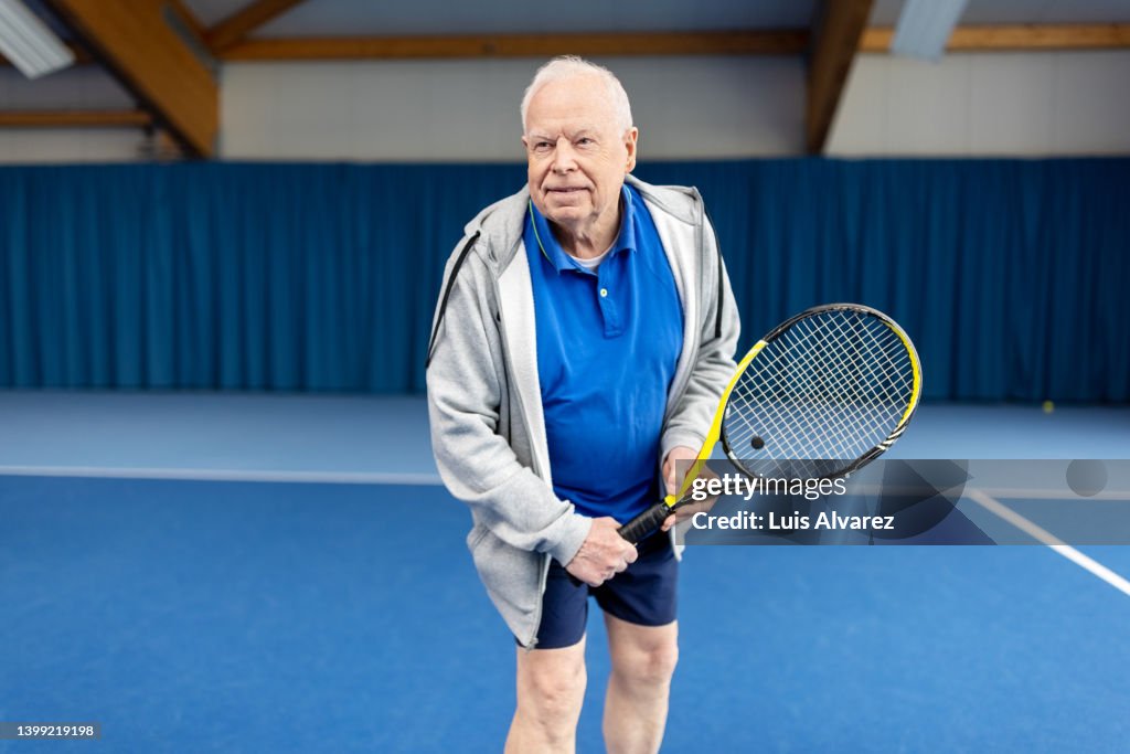 Senior male in sportswear playing tennis on indoor court