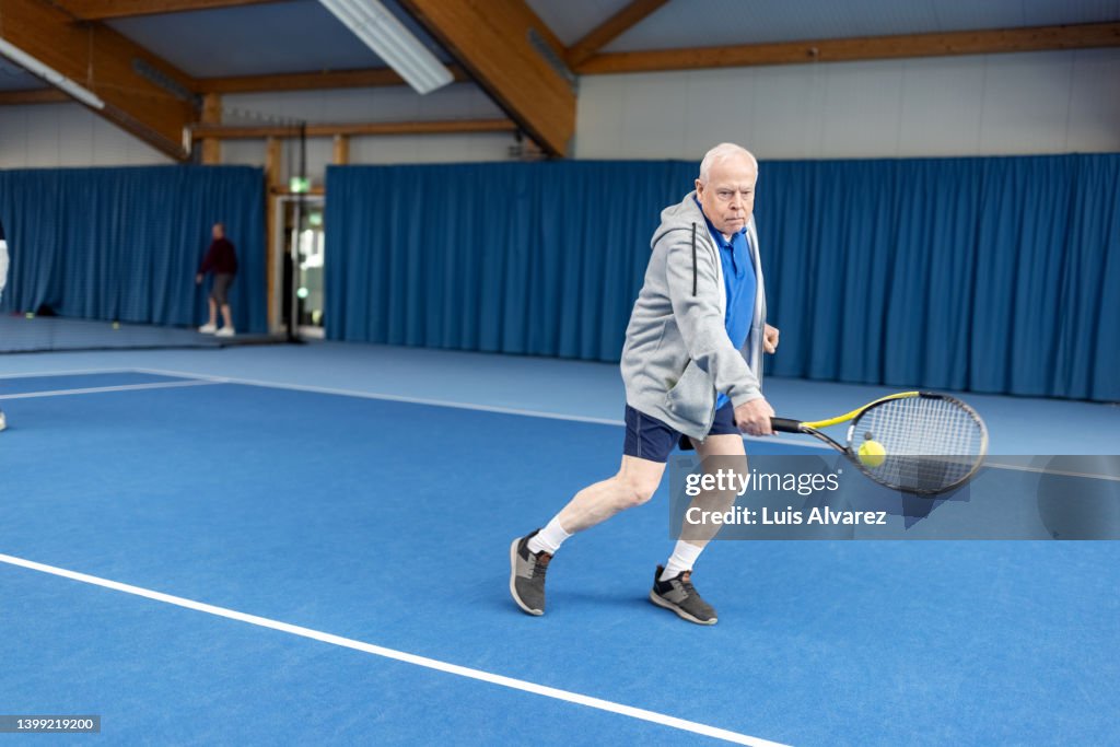 Senior man playing tennis on indoor court