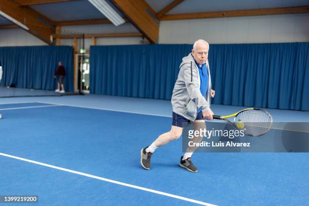 senior man playing tennis on indoor court - 80s tennis players stock pictures, royalty-free photos & images