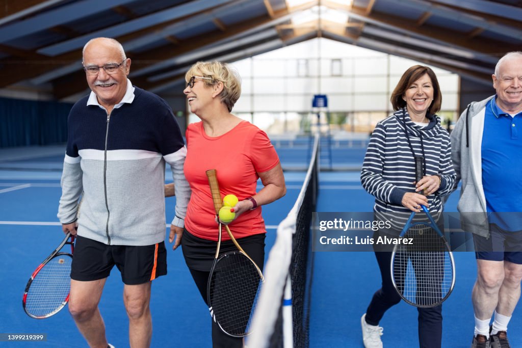 Happy senior couples walking on tennis court after the game
