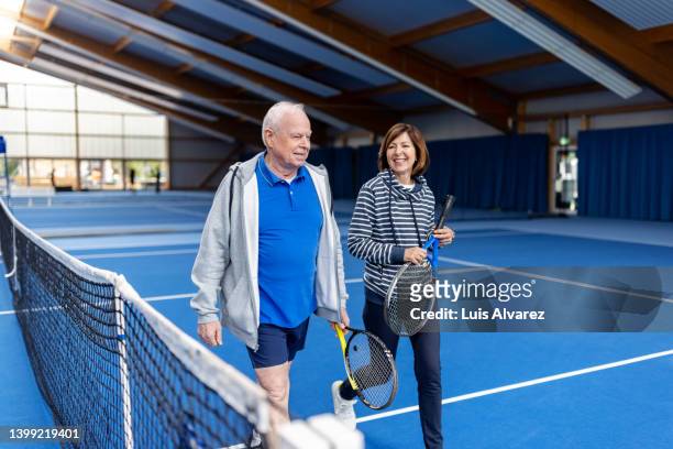 active senior couple in sportswear walking on indoor tennis court - 80s tennis players stock pictures, royalty-free photos & images