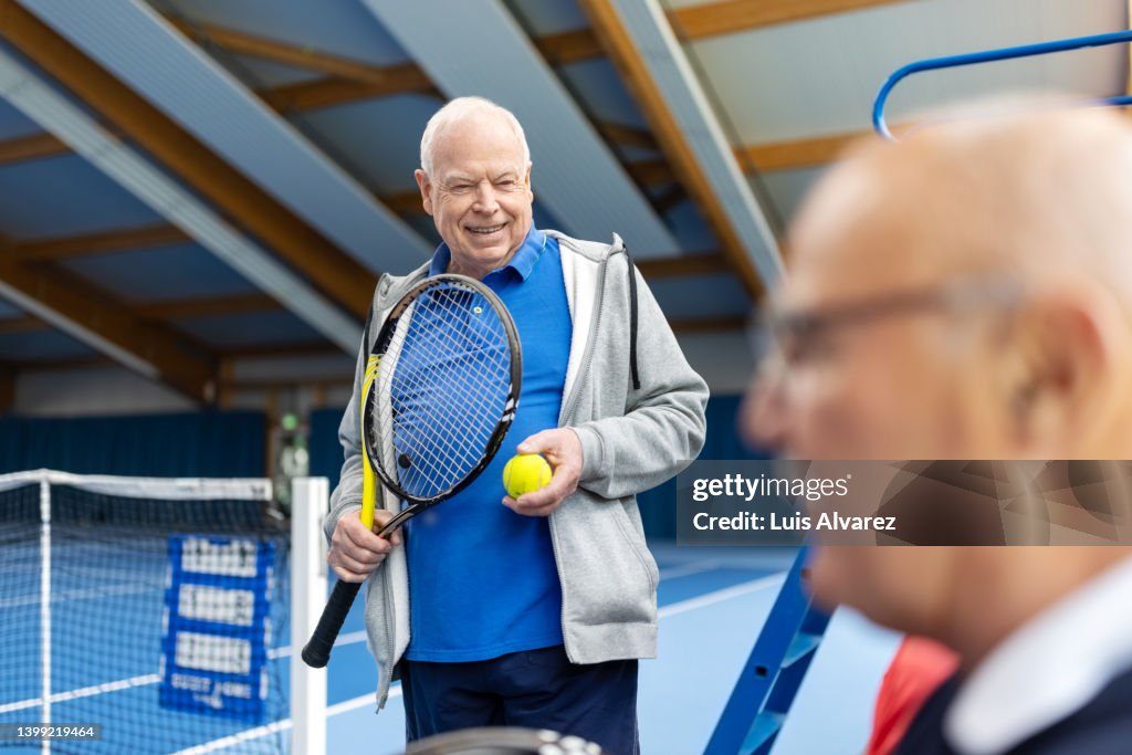 Cheerful senior men taking a break from tennis and talking on court