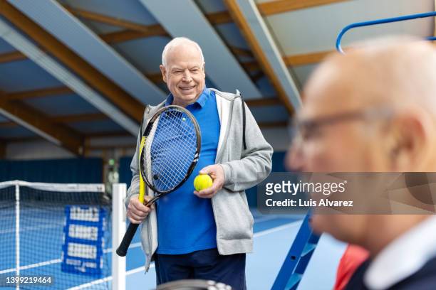 cheerful senior men taking a break from tennis and talking on court - 80s tennis players stock pictures, royalty-free photos & images