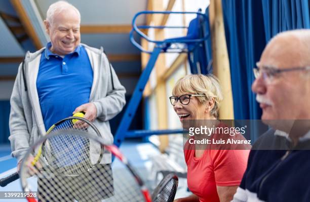 senior friends taking a break from the tennis game and talking on indoor tennis court - 80s tennis players stock pictures, royalty-free photos & images