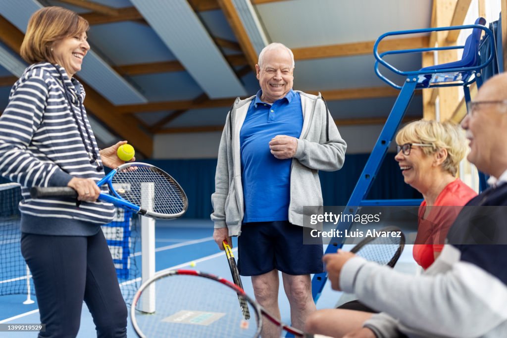 Cheerful senior friends taking a break from tennis game on indoor court