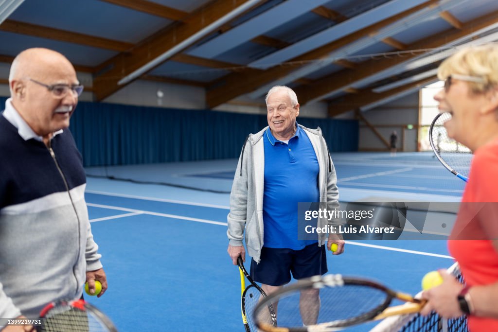 Healthy senior people talking near the net on tennis court