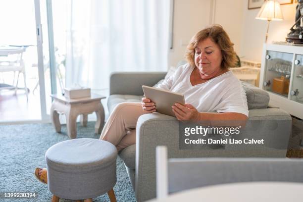 senior woman relaxing on the sofa and using a digital tablet - widow stock pictures, royalty-free photos & images