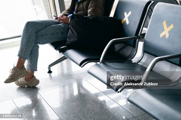 a sticker with a yellow symbol placed on a chair at the airport, a distance of one seat from other people. keeping a distance, preventing the risk of spread from covid-19, coronavirus. a woman is waiting for departure with a phone in her hands. - mobile on plane stock pictures, royalty-free photos & images