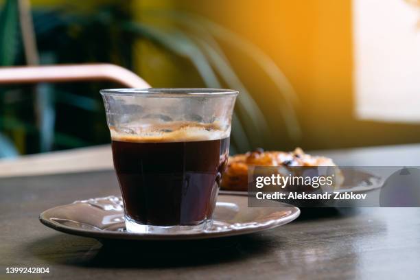 a mug of black coffee or americano, a croissant or a bun with raisins on a plate at the dining table in a cafeteria, restaurant, cafe or bakery. the concept of a coffee break, breakfast. fresh pastries. - americano photos et images de collection