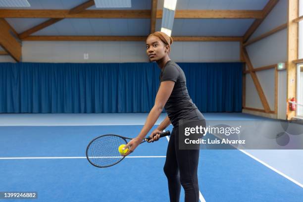 african woman serving a ball on indoor tennis court - schlägersport stock-fotos und bilder