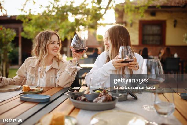 close-up portrait of two female friends in strict suits laughing drinking wine on the terrace outside at summer street cafe - restaurant patio stockfoto's en -beelden