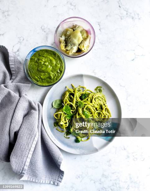 plate of spaghetti with pesto, and two bowls of artichokes, and pesto sauce on white, marble background - pistou photos et images de collection