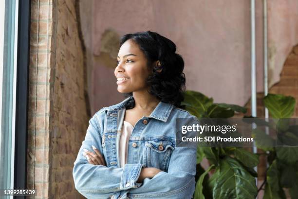 confident young woman looks out window - girl in office stock pictures, royalty-free photos & images