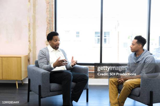 mid adult male counselor gives young man advice - psychotherapy imagens e fotografias de stock