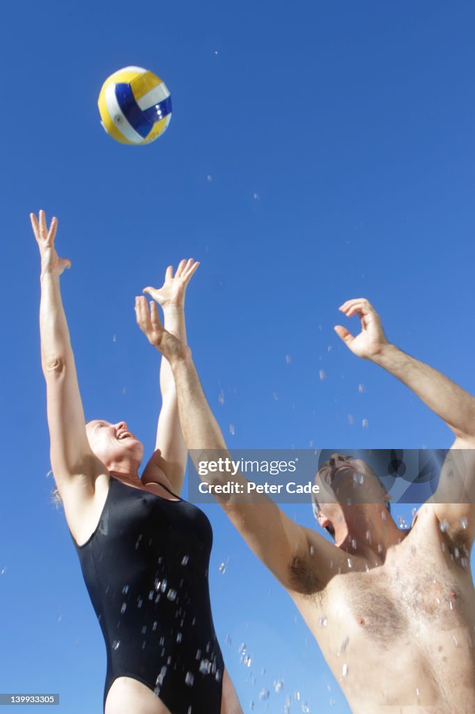 Couple in pool jumping for ball