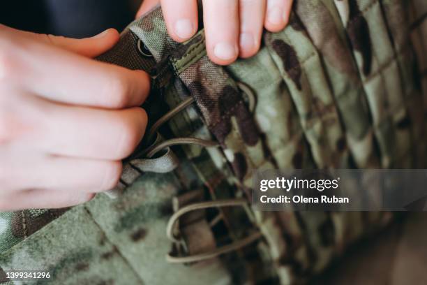 female hands adjusting tactical load bearing vest. - khaki green stock-fotos und bilder