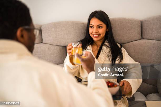 gorgeous latina woman wearing a bathrobe and having breakfast in bed with her husband - indulgence stock pictures, royalty-free photos & images