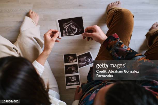 couple sitting on the ground watching ultrasound. - new baby fotografías e imágenes de stock