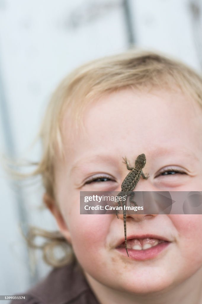 Toddler girl smiles at camera with Sagebrush lizard on nose in Chico, California.