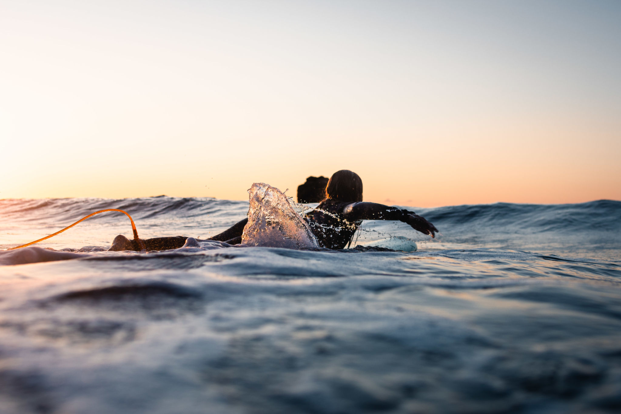 Low angle view of a surfer girl seen from behind. Paddling on a board in the water Low angle view of a surfer girl seen from behind. Paddling on a board in the water