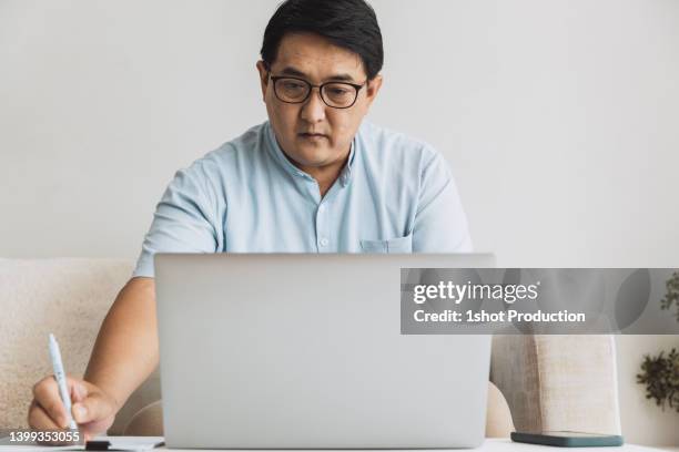 mature man working at home using laptop in living room. - vpn stock pictures, royalty-free photos & images