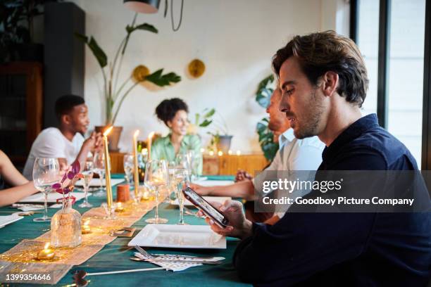 giovane che legge un messaggio di testo durante una cena con gli amici - shy foto e immagini stock