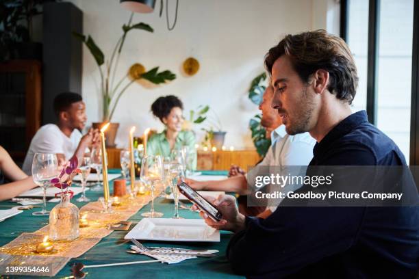 young man reading a text message during a dinner party with friends - verlegen stockfoto's en -beelden