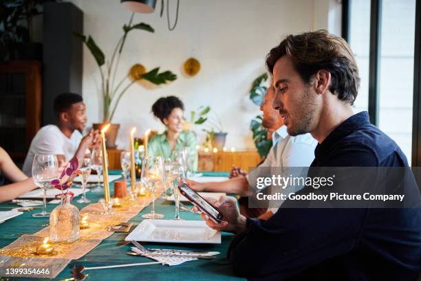 young man reading a text message during a dinner party with friends - no confidence stock pictures, royalty-free photos & images