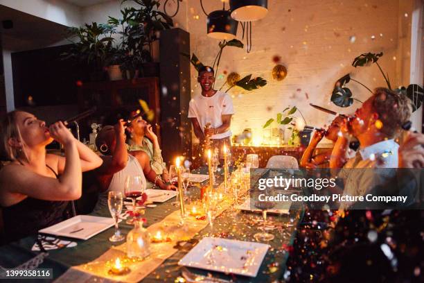 confetti falling on friends blowing party horns during a new year's eve party - men of the year party inside stock pictures, royalty-free photos & images