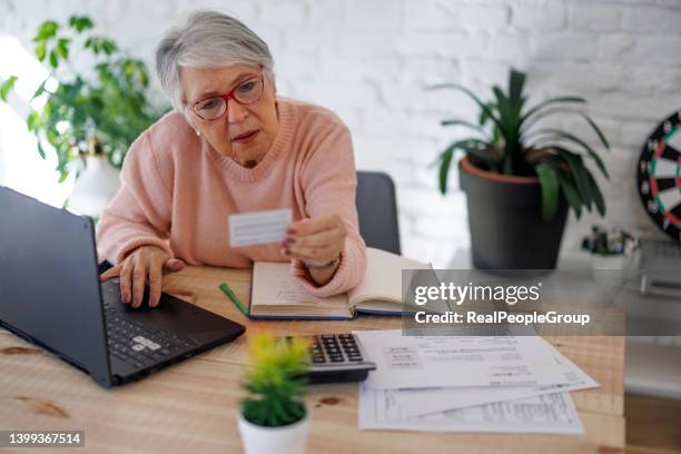 portrait of senior happy stylish woman with grey hair making online shooping using laptop with credit card indoor.cheerful elderly lady with credit card smiling and using laptop while sitting at table and doing online shopping at home - retirement card stock pictures, royalty-free photos & images