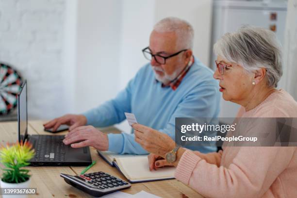 senior woman holding credit card and using laptop computer while paying bills at home with credit card. - retirement card stock pictures, royalty-free photos & images