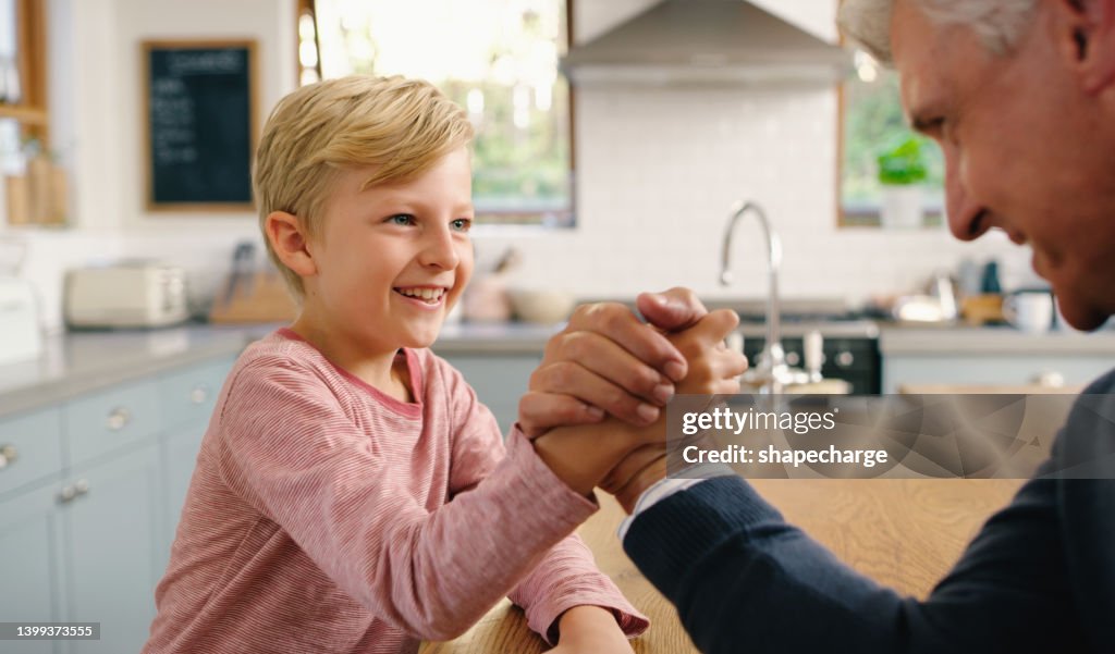 Grandfather and grandson having an arm wrestle at home. Cute and smiling little boy child having family fun and sharing a playful moment with his senior relative