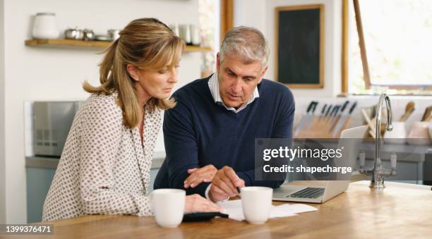 a senior couple planning their finance and paying bills while using a laptop at home. a mature man and woman going through paperwork and working online with a computer - 50s woman writing at table imagens e fotografias de stock