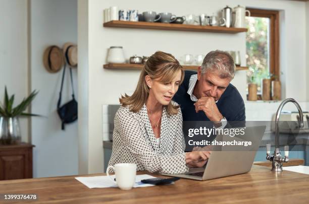 una pareja de personas mayores que planifica sus finanzas y paga facturas mientras usa una computadora portátil en casa. un hombre y una mujer maduros que pasan por el papeleo y trabajan en línea con una computadora - buscador fotografías e imágenes de stock