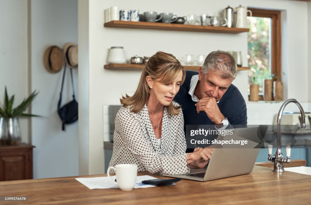 A senior couple planning their finance and paying bills while using a laptop at home. A mature man and woman going through paperwork and working online with a computer