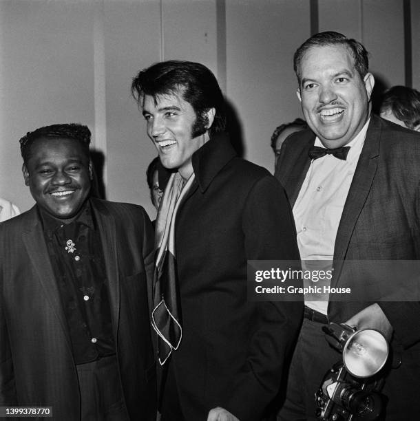 American singer-songwriter and pianist Fats Domino , American singer and actor Elvis Presley , wearing a black jacket with a red-and-black scarf, and...