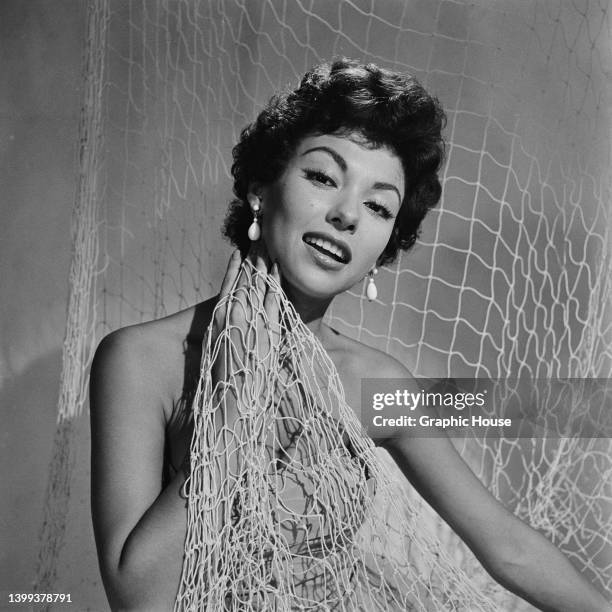 Puerto Rican singer, dancer and actress Rita Moreno, wearing a strapless bathing costume, posing with a fishing net in a studio portrait, circa 1950.