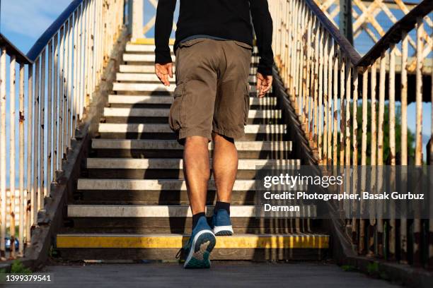 rearview of a man climbing up the stairs of a footbridge - pantalón corto fotografías e imágenes de stock