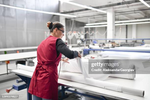 vista trasera de una trabajadora textil experta que desenrolla rollos de material para cortar - textile industry fotografías e imágenes de stock