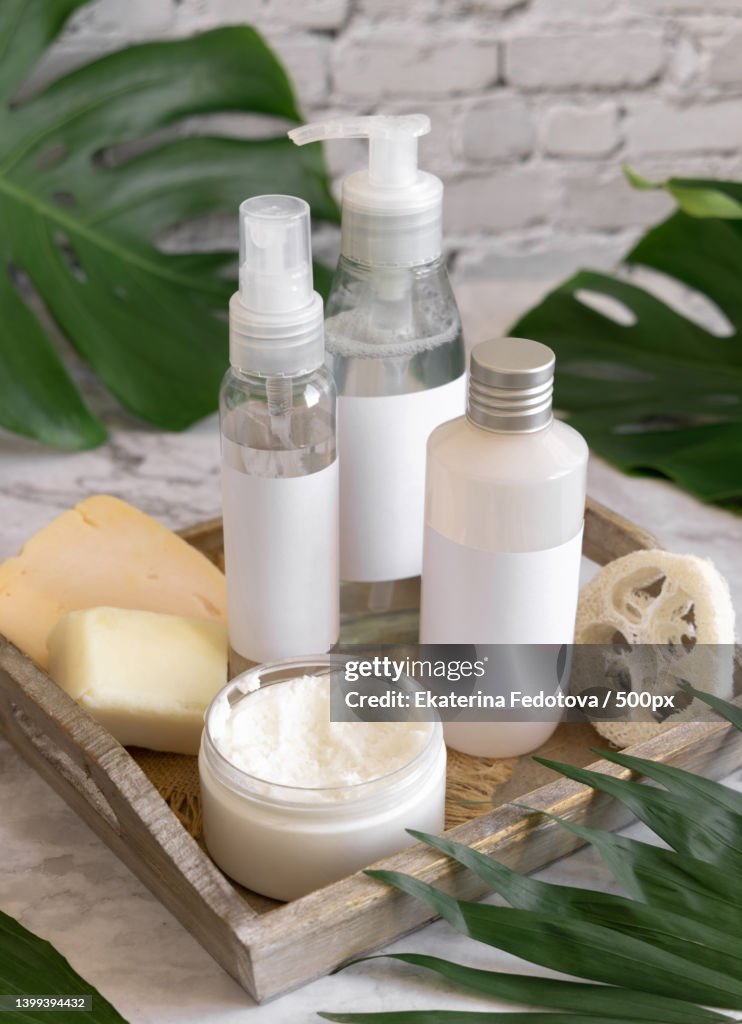 Cosmetic bottles and skin care accessories near monstera leaves close up Brand packaging mockup