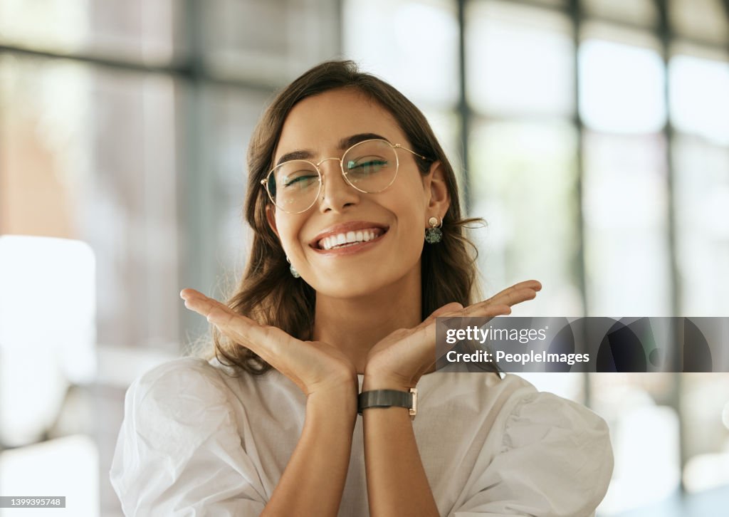 Cheerful business woman with glasses posing with her hands under her face showing her smile in an office. Playful hispanic female entrepreneur looking happy and excited at workplace