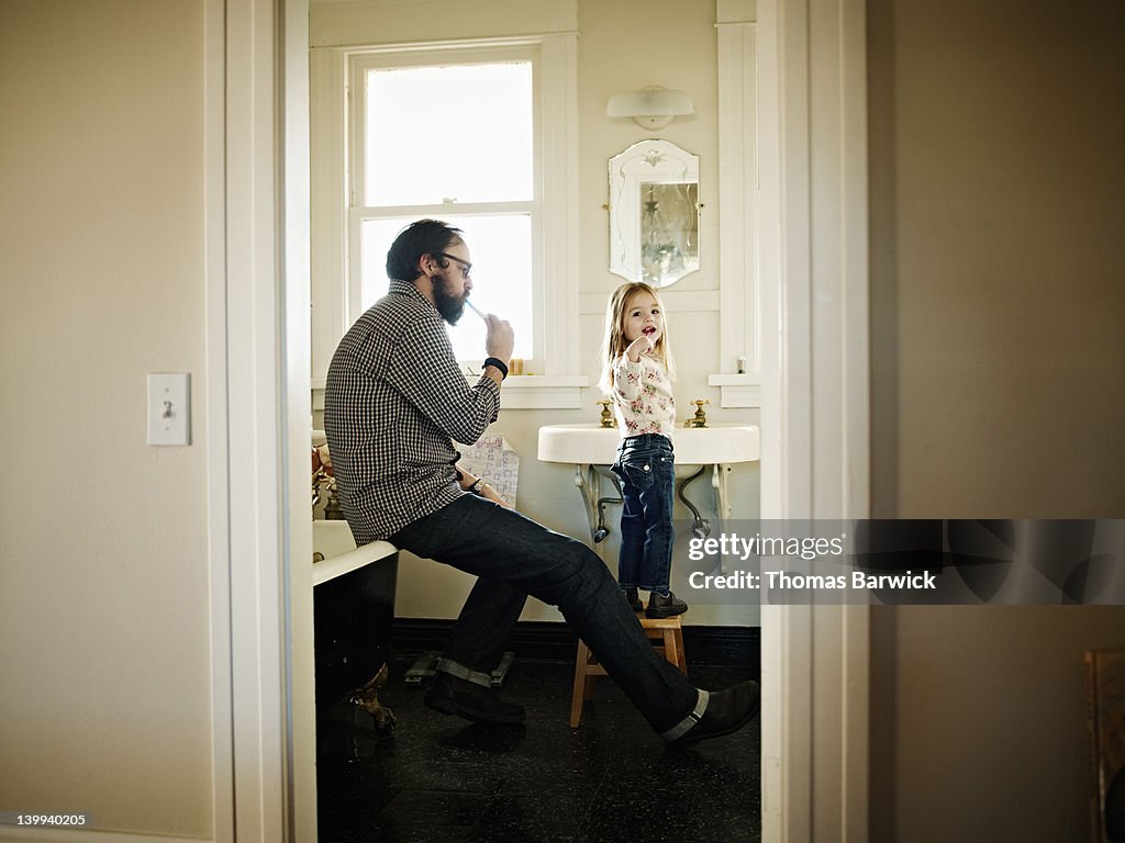 Father and daughter brushing teeth in bathroom