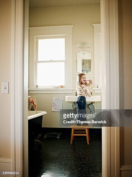 Young girl standing on stool brushing teeth