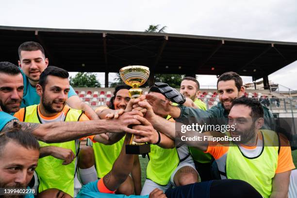 team players are touching their trophy to celebrate together - football team trophy stock pictures, royalty-free photos & images
