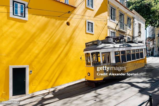 yellow tram moving past yellow building in lisbon, portugal - lissabon stockfoto's en -beelden